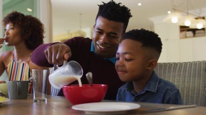 非裔美国父亲在家里向儿子倒麦片碗中的牛奶时微笑