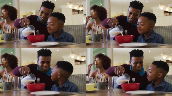 非裔美国父亲在家里向儿子倒麦片碗中的牛奶时微笑