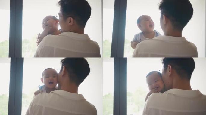 父亲抱着并亲吻可爱的新生男婴，看着窗外。单身父母，真实的生活方式育儿父亲时刻