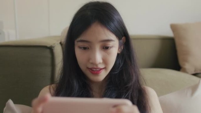 亚洲女人拿着智能手机在客厅玩游戏。