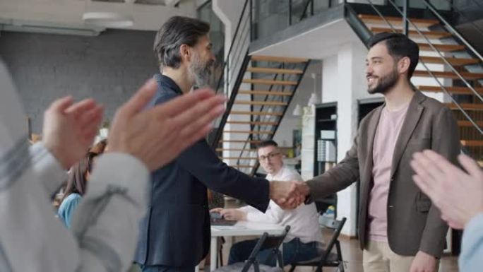 当人们在工作场所鼓掌时，经理与男性员工握手祝贺
