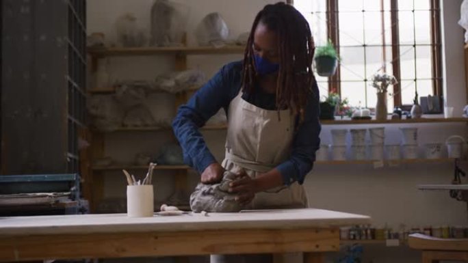 戴着口罩和围裙的女陶工在陶艺工作室揉捏粘土