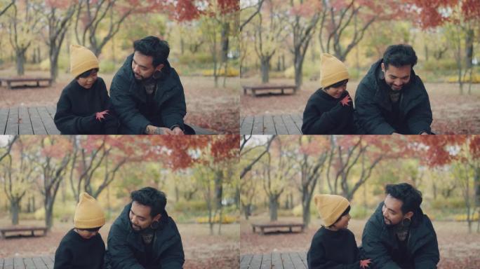 父亲和儿子说话，坐在秋公园的长凳上。