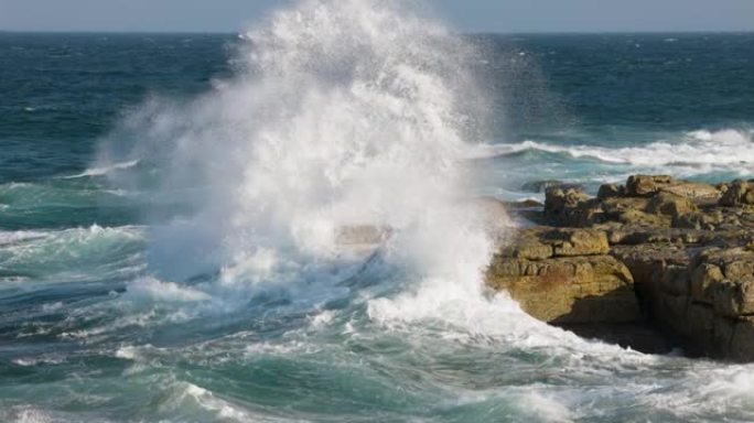 在岩石海岸线上冲破岩石的波浪的空中慢动作视图