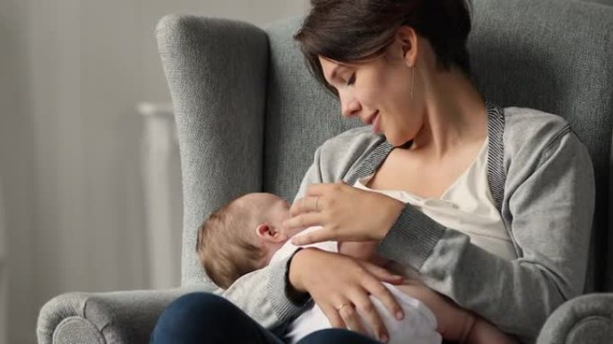 年轻女子坐在舒适的扶手椅上母乳喂养她的新生婴儿