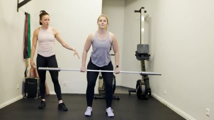 女人在健身房用杠铃和健身教练一起锻炼