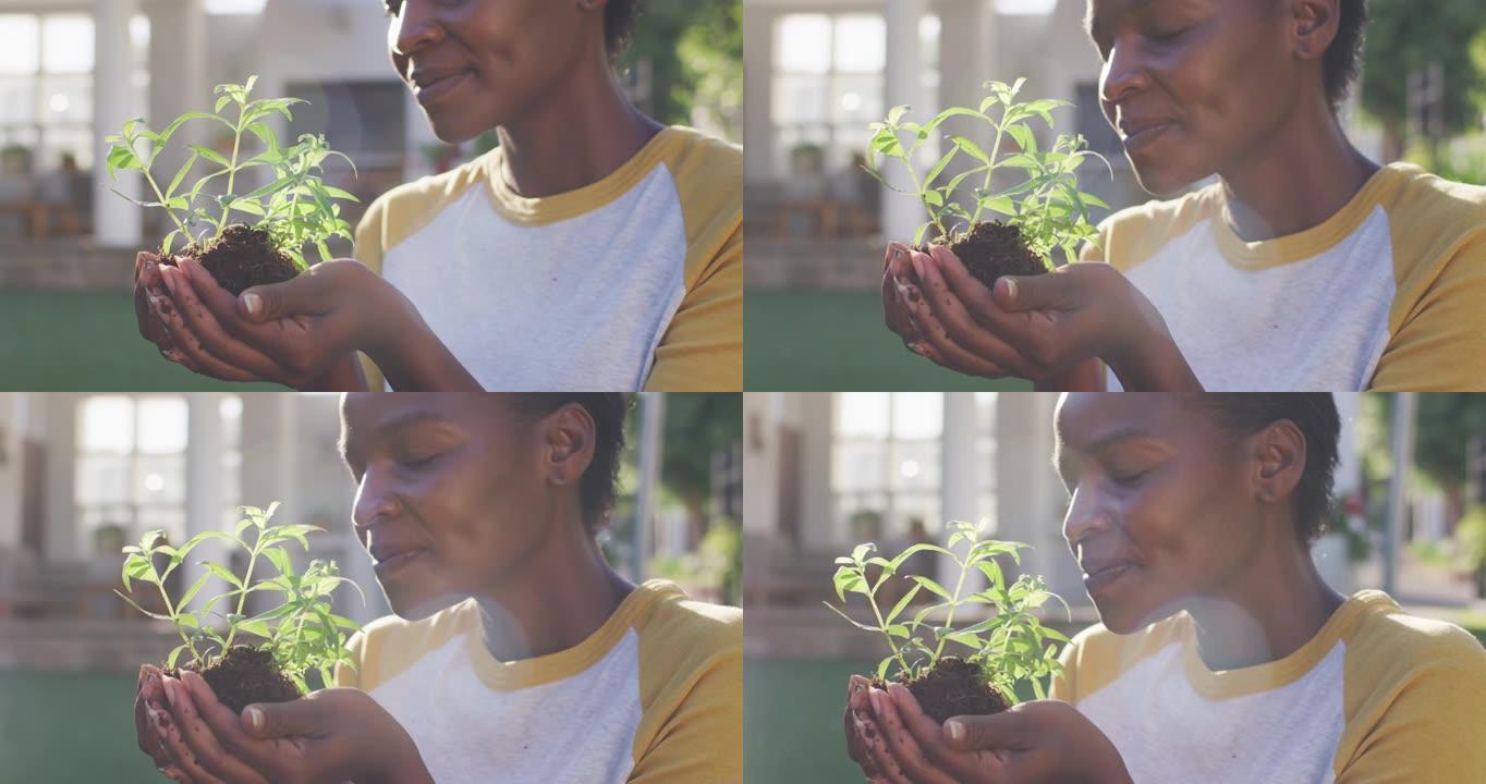 快乐的非洲裔美国女性园艺，在花园里拿着和闻到植物
