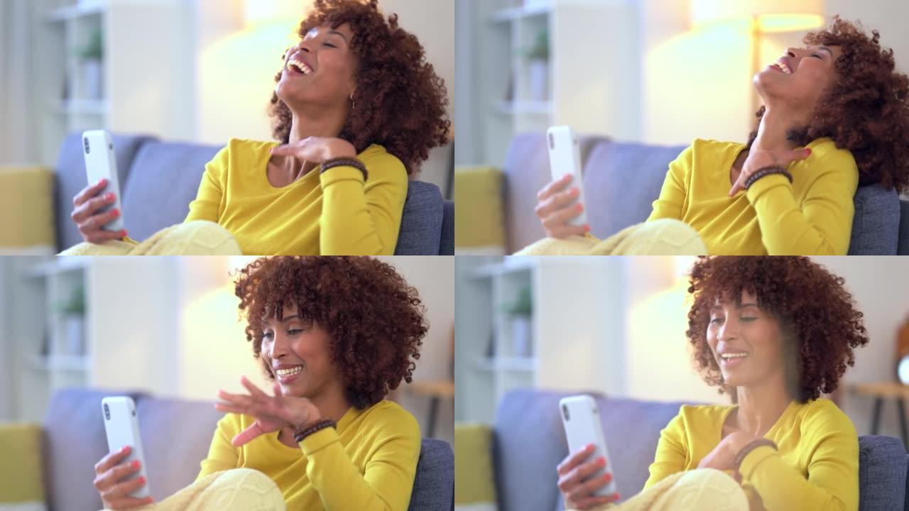 开朗的女人在视频通话中聊天，在家里的沙发上放松时大笑。时尚的非洲女性在与远方朋友或家人的电话中有趣的