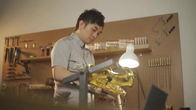 亚洲华人男子在车间检查和修理萨克斯管音乐管乐器