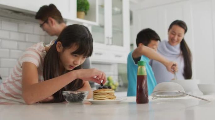 快乐的亚洲父母与儿子和女儿一起在厨房做饭，女儿将浆果放在煎饼上