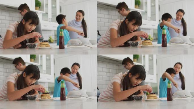 快乐的亚洲父母与儿子和女儿一起在厨房做饭，女儿将浆果放在煎饼上