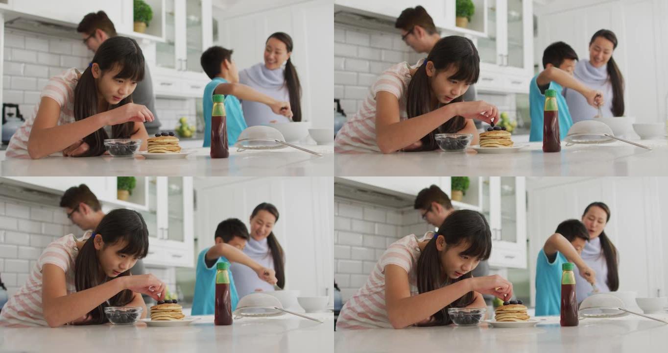 快乐的亚洲父母与儿子和女儿一起在厨房做饭，女儿将浆果放在煎饼上