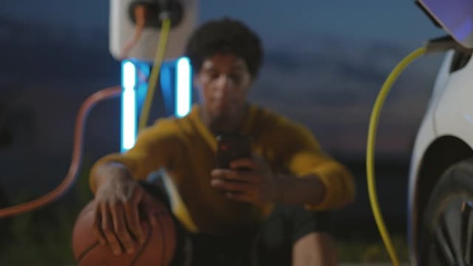 篮球运动员使用智能手机并在充电后拔下EV插头的肖像