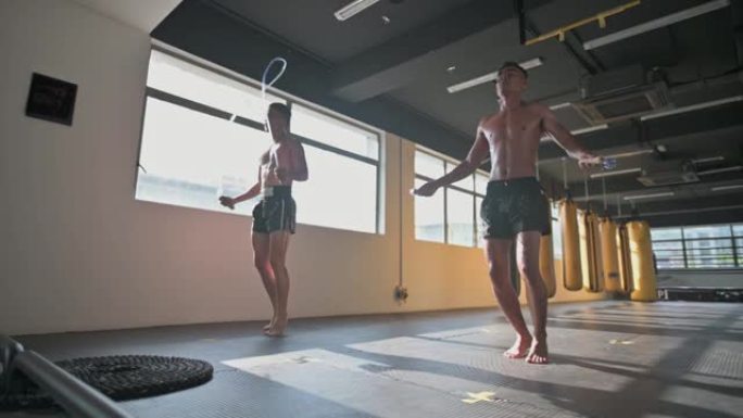 亚洲男运动员跳绳健身俱乐部用一排黄色出气筒沙袋在窗口白天时间