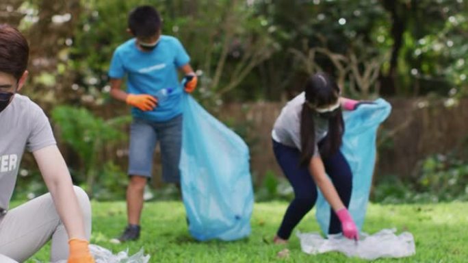 亚洲父母，儿子和女儿戴着口罩，拿着垃圾袋收集塑料垃圾