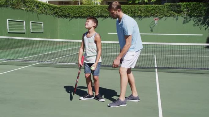 白种人父亲在晴朗的晴天教儿子在网球场打网球