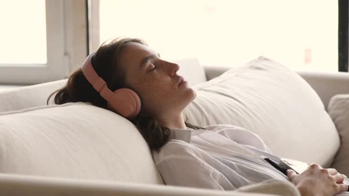 放松的女人戴着耳机在手机上听播放列表最喜欢的音乐