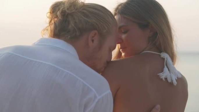 25-29岁的拉丁美洲和西班牙裔夫妇在沙滩上沿着日落海的边缘浪漫接吻。家庭假期快乐。非高加索蜜月概念
