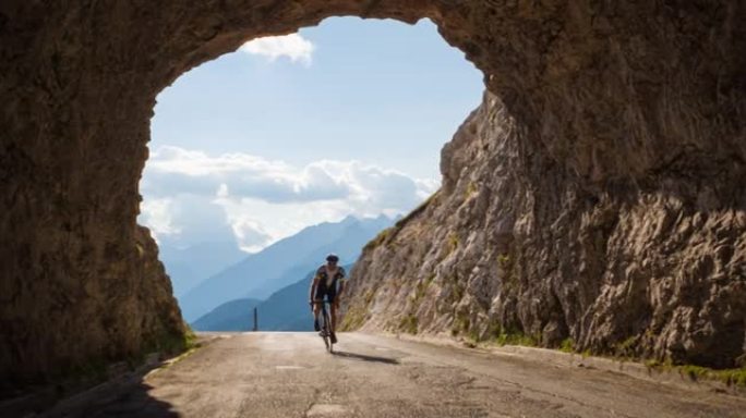 坚定的公路自行车手骑在山路上，穿过岩石隧道