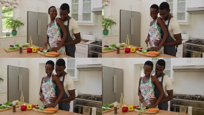 微笑的非洲裔美国夫妇穿着围裙在厨房里拥抱和准备食物