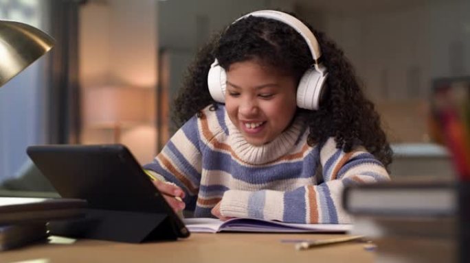 4k视频片段，一个年轻女孩坐在家里，戴着耳机，同时使用平板电脑进行电子学习