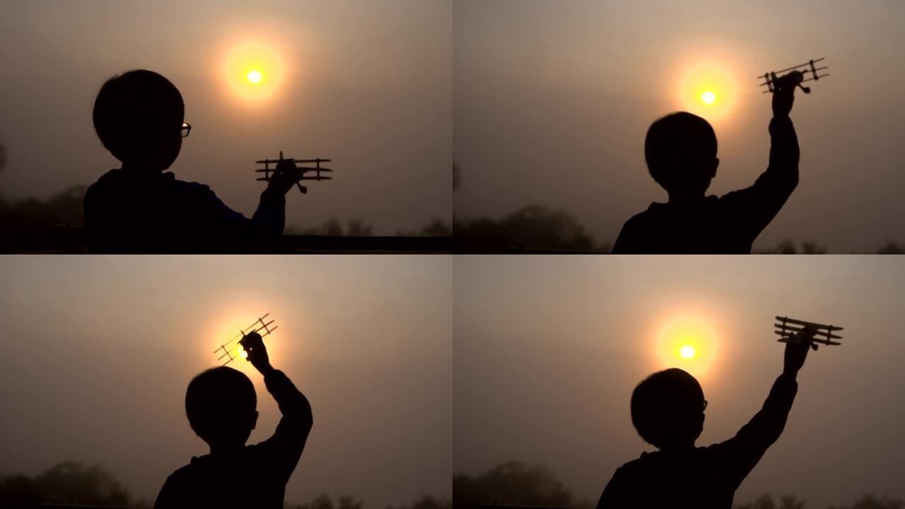 一个男孩的轮廓，一个玩具飞机站在早晨的阳光下。