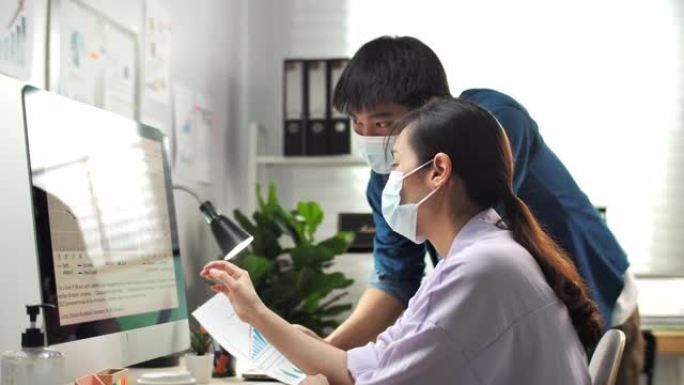两位亚洲商务人士同事一起在现代化办公室的电脑上集思广益