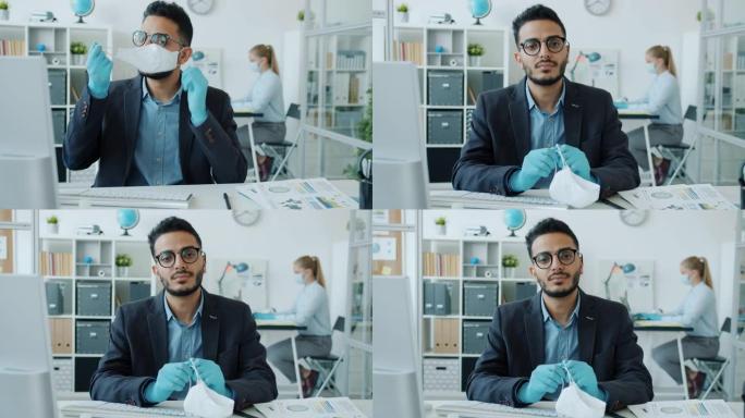阿拉伯男人脱下医用口罩的肖像坐在办公室的办公桌上看着相机