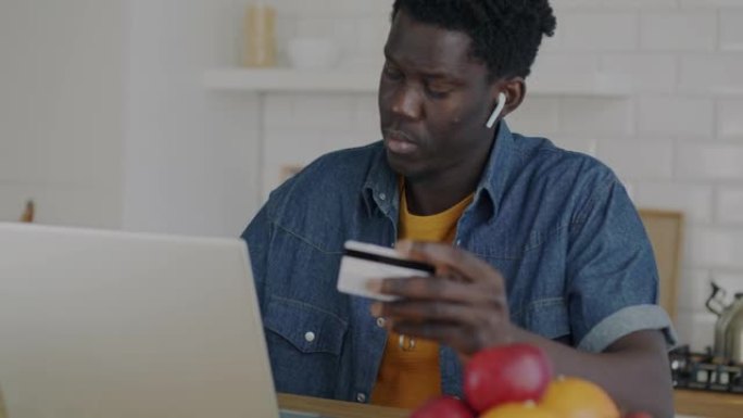 非裔美国人在家里的厨房里用笔记本电脑用信用卡在线支付