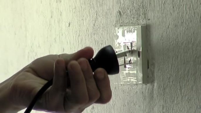 男性手将三针插头连接到墙壁插座。特写。