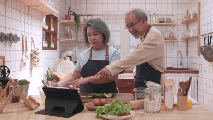 老年夫妇正在学习如何使用平板电脑在厨房中烹饪食物，表达了他们对他们的持久爱。以及退休后的幸福，是通过