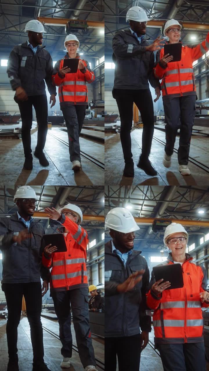 两名重工业工程师站在钢铁金属制造厂，使用数字平板电脑并进行讨论。黑人工业专家与女技术员交谈。垂直屏幕