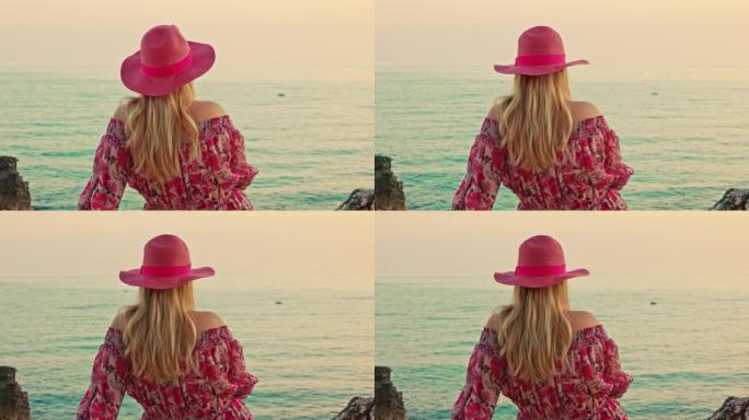 赫瓦岛 (Hvar island) 傍晚坐在海边的金色头发，粉红色帽子和连衣裙的女人