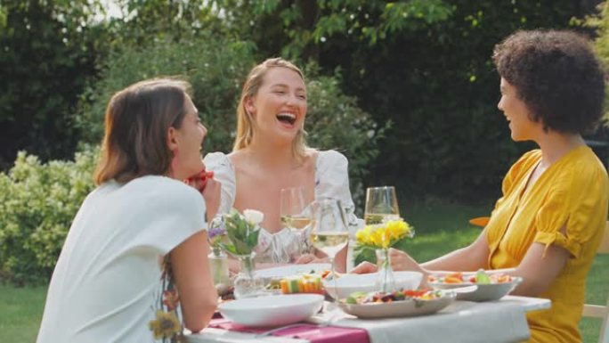 三个女性朋友坐在夏天的花园里吃饭喝酒，一边聊天，一边追赶慢动作