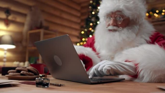 圣诞老人正在视频聊天，使用他的笔记本电脑，而相机将他从一侧拍摄到另一侧