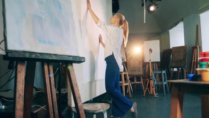 创造，灵感概念。金发碧眼的女士正在工作室里触摸一块巨大的白色画布。创意爱好，艺术品生物概念。