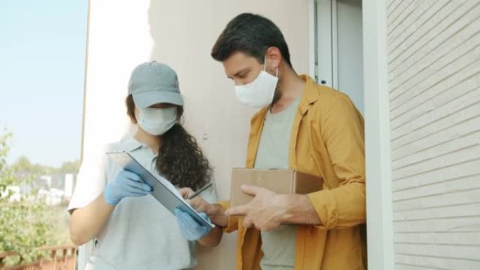 穿着医用口罩和手套的送货员和顾客在户外谈论拿着包裹签字纸