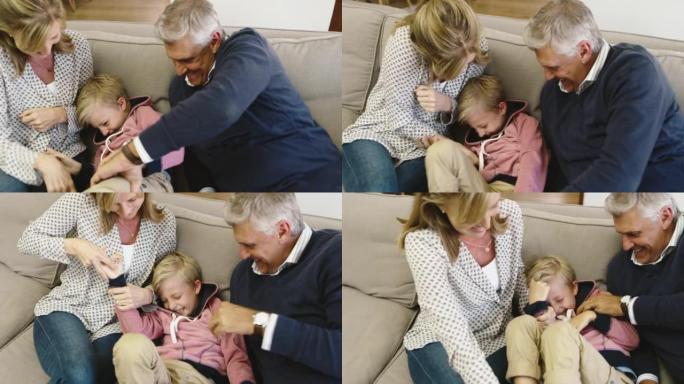家庭在家里玩得开心。一个高级男人和女人在挠他们的小男孩。爷爷奶奶和可爱的孙子在沙发上玩耍
