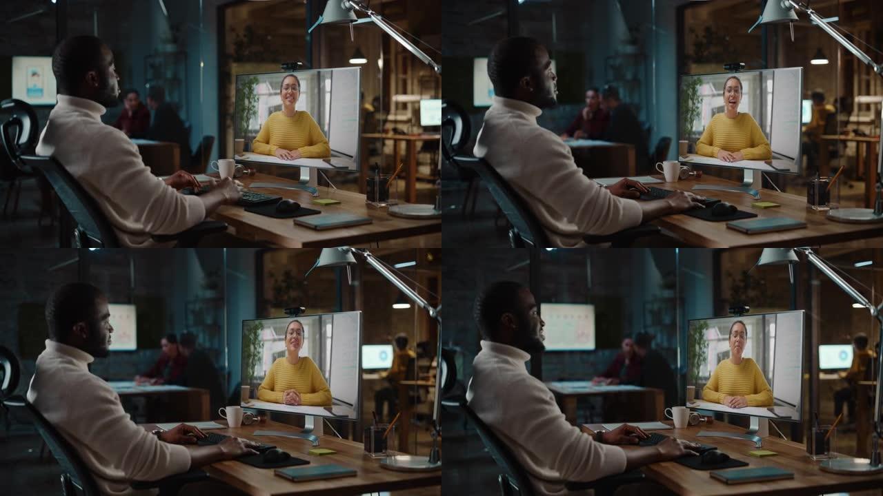 英俊的黑人非洲裔美国项目经理正在创造性的办公环境中，在台式计算机上进行视频通话。男性专家通过实时摄像