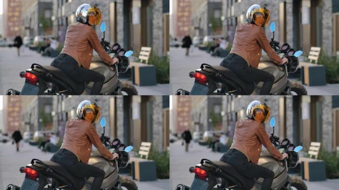 穿着皮夹克的迷人骑自行车的女人戴着头盔坐在运动摩托车上。性感的司机女孩坐在城市的摩托车上转身。美丽的