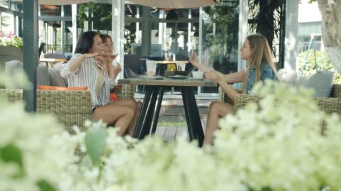 无忧无虑的女人在户外咖啡馆跳舞，而女性朋友录制视频并大笑