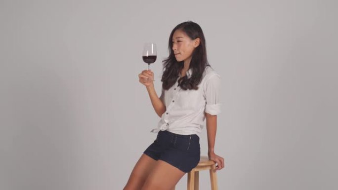 亚洲中国美女牙托坐在椅子上喝着灰色背景微笑的红酒