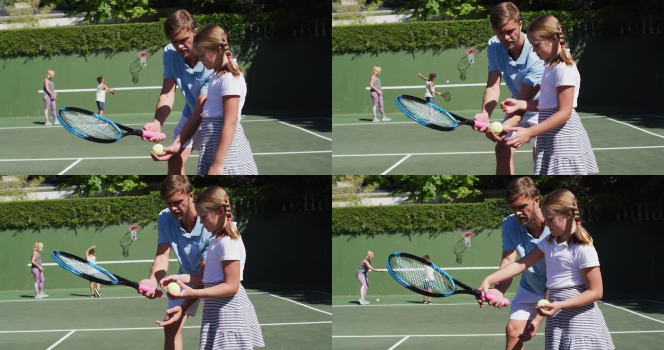 白人父亲在阳光明媚的日子里教女儿在网球场打网球