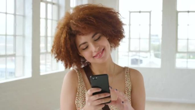 时尚的红发女人在手机上阅读浪漫的短信。一位时尚时尚的女性在使用社交媒体时微笑着思考。体贴的年轻女孩使