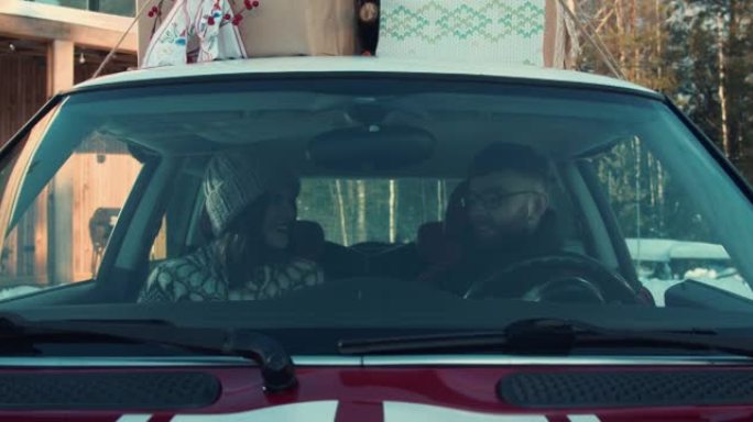 快乐的年轻开朗的浪漫情侣坐在漂亮的红色新车里微笑着兴奋地交谈。圣诞节呈现慢动作。