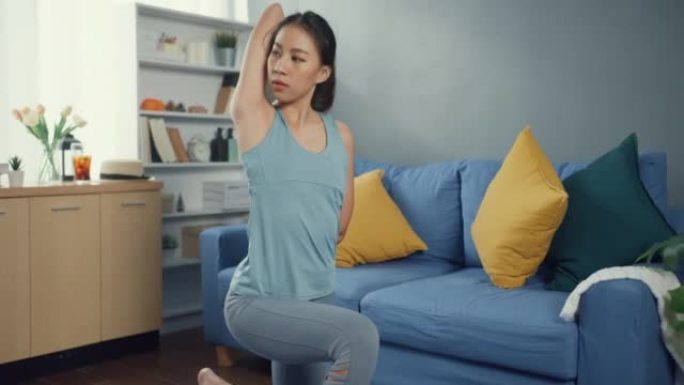 年轻迷人的运动亚洲强壮的女人穿着运动服，感觉平静，在家里的客厅为初学者热身练习瑜伽。家庭检疫锻炼和健