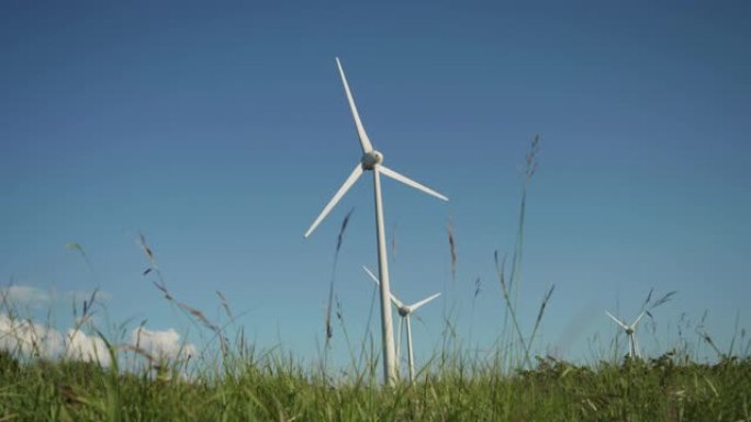 风力涡轮机旋转并产生可持续生态能源的地面射击。风车在绿色领域生产清洁可再生能源。背景与美丽晴朗的夏天