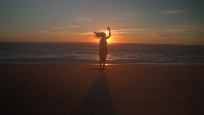 WS日落时在海滩上跳舞的年轻女子的剪影