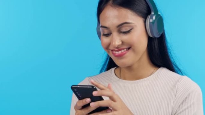 美丽的年轻混血女子一边用手机一边耳机听音乐。快乐混血模特儿戴耳机，透过音乐浏览