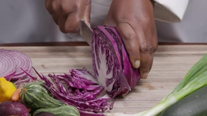 非洲黑人厨师的双手在被其他蔬菜包围的砧板上切白菜的短视